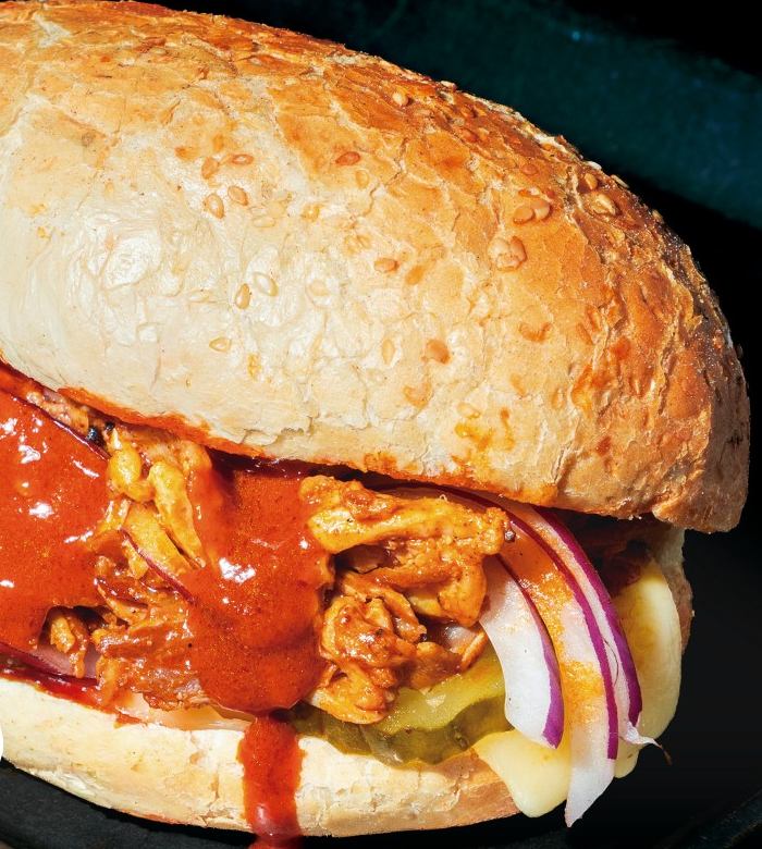 Kebab La Brava de Jekes en primer plano: pan de kebab con sésamo, carne de ternera y pollo con salsa brava, queso fundido, pepinillos y cebolla morada.